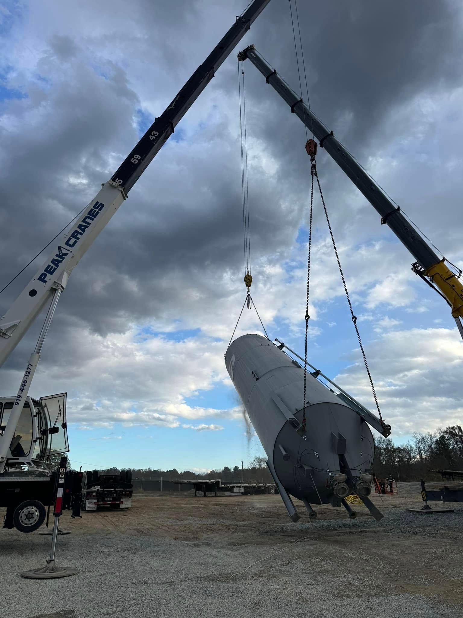 A crane is lifting a large object in a gravel lot.