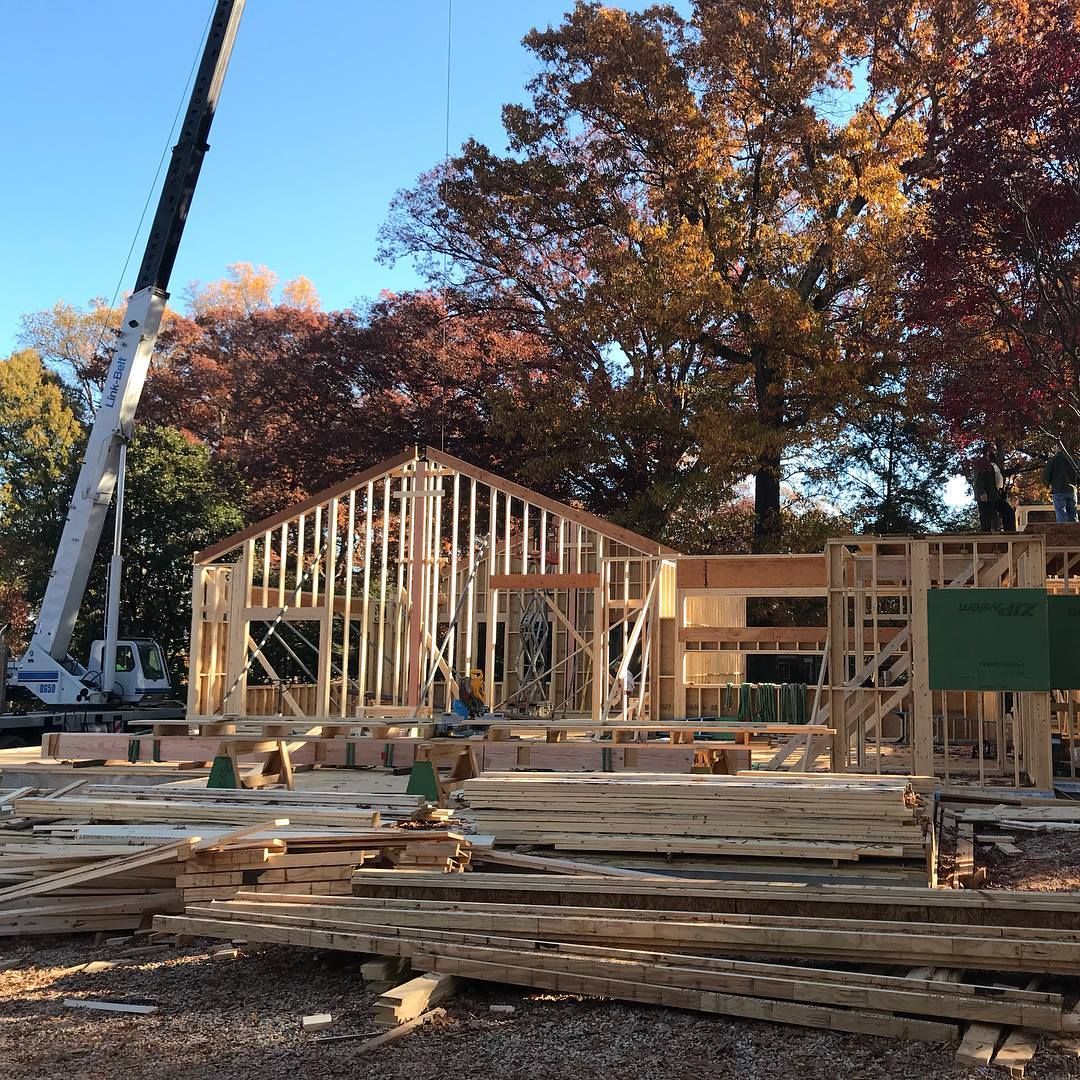 A large pile of wood is sitting in front of a house under construction.