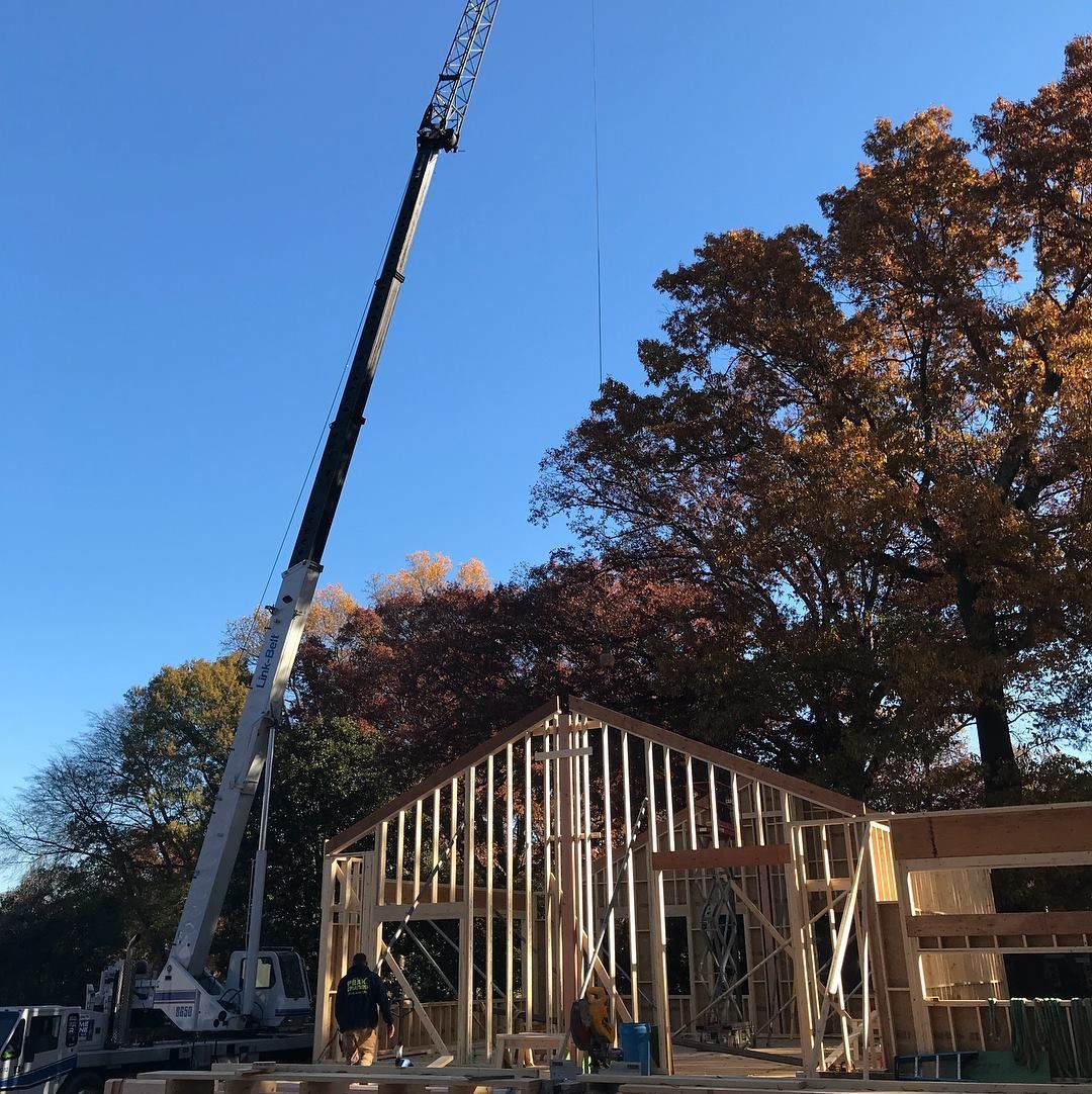 A crane is lifting a house frame in the air