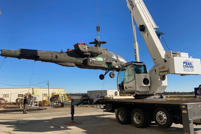 A large military helicopter is being lifted by a crane