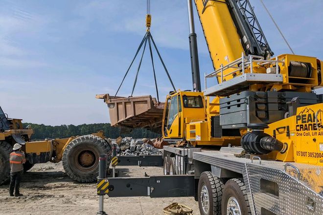 A large yellow crane is lifting a large bucket on top of a truck.
