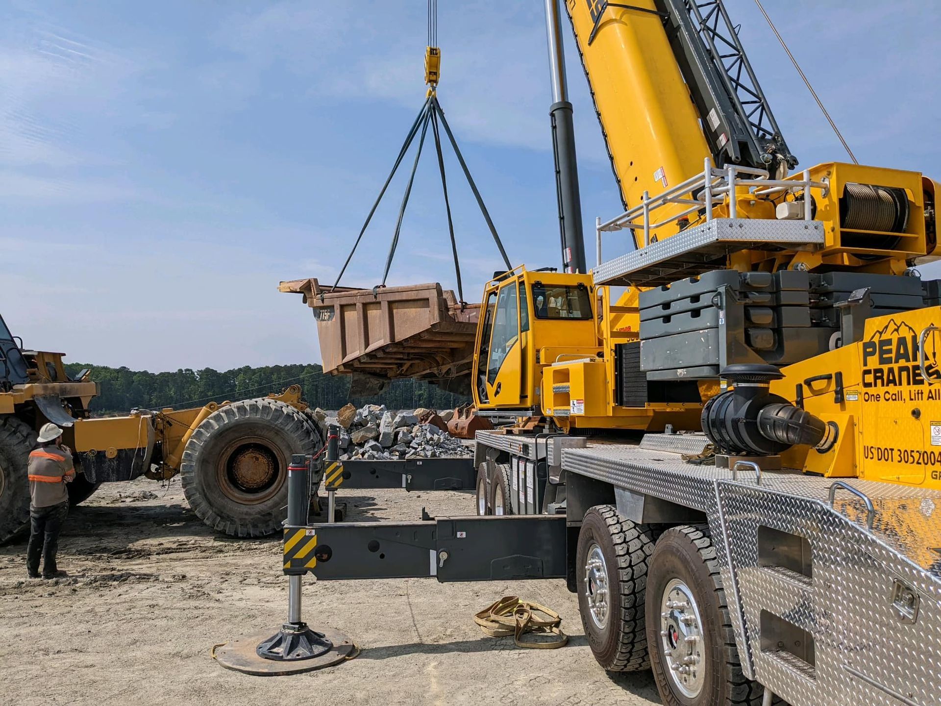 A large yellow crane is lifting a dump truck.