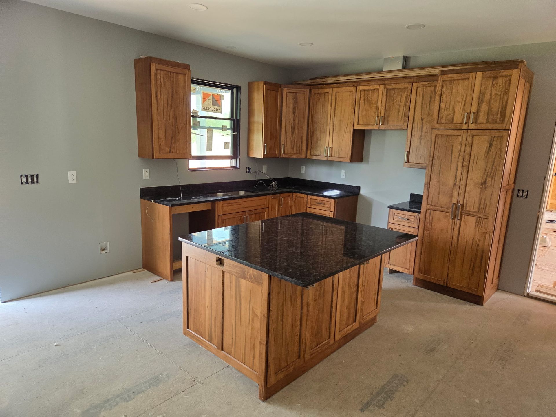 Unfinished kitchen with wood cabinets, black island countertop, and beige carpet flooring.