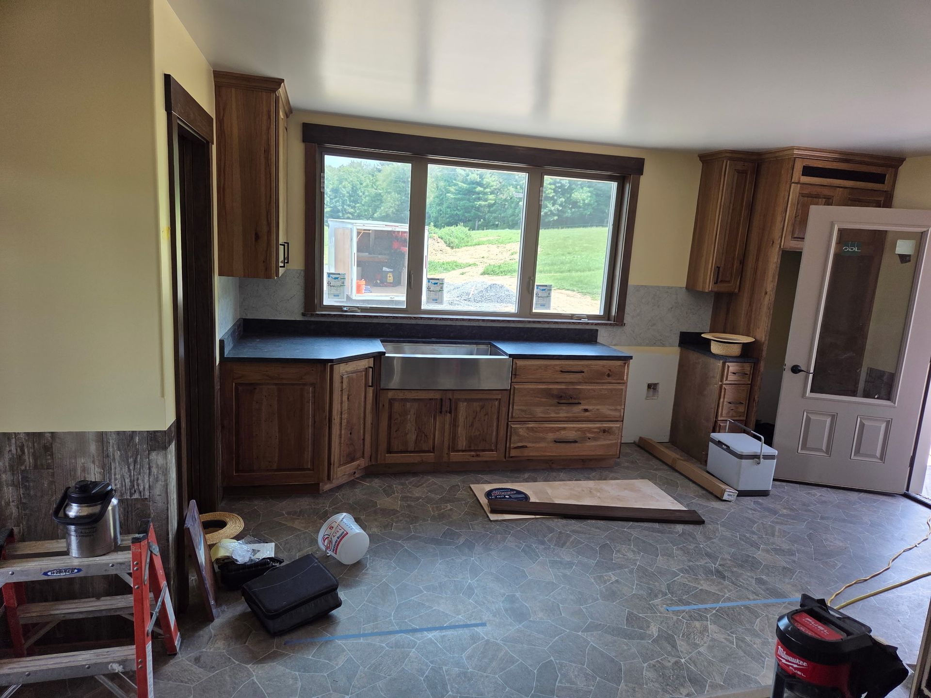Partially renovated kitchen with wooden cabinets, large window, and construction materials on the floor