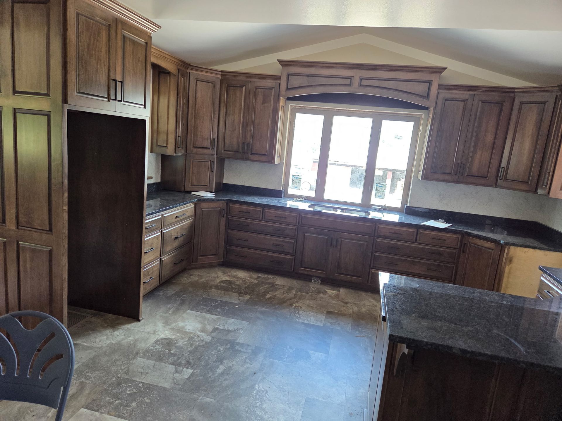 Wood-paneled kitchen with dark cabinets, black countertops, and a large window above the sink.