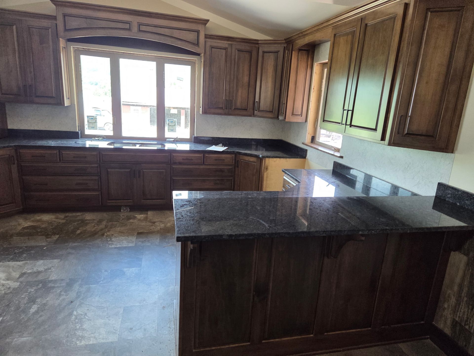 Empty kitchen with dark wood cabinets, black countertops, and a window above the sink.