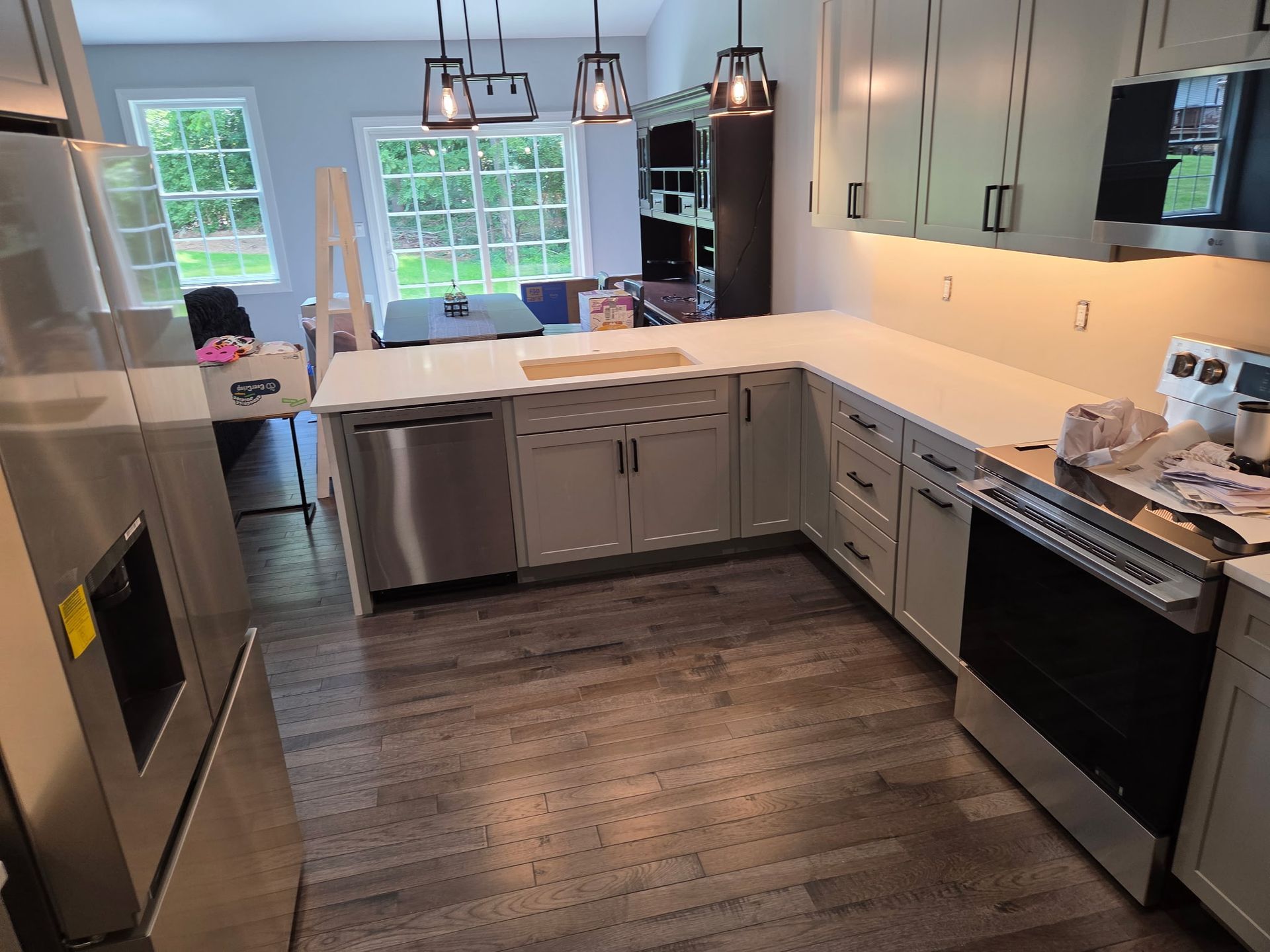 Modern kitchen with stainless steel appliances, white cabinets, island, and large windows overlooking a backyard