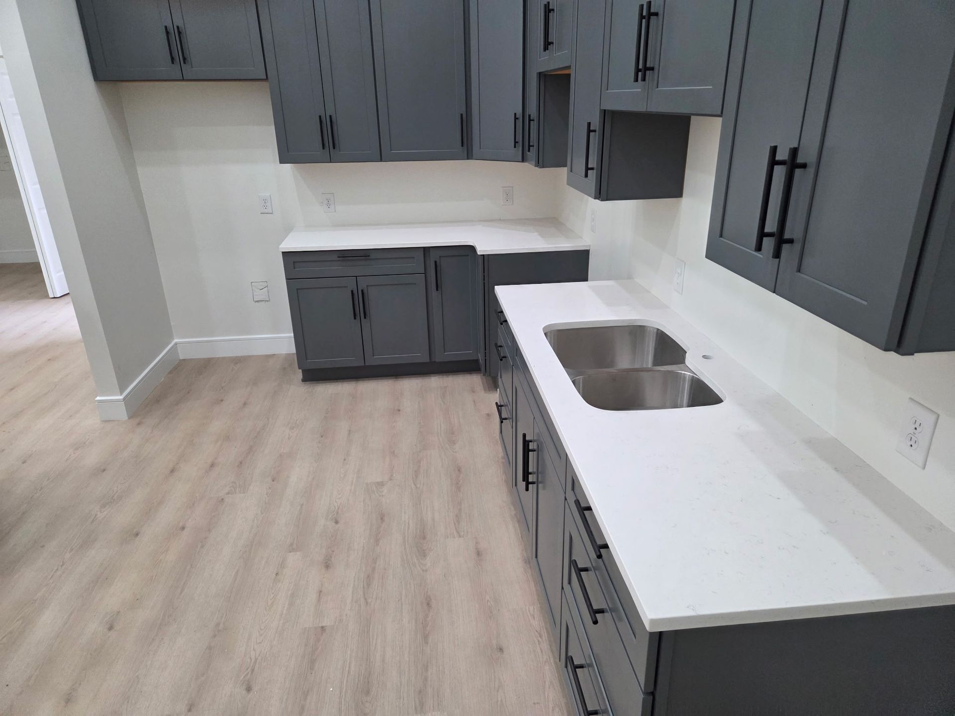 Modern kitchen with gray cabinets, white countertops, and a double sink on light wood flooring