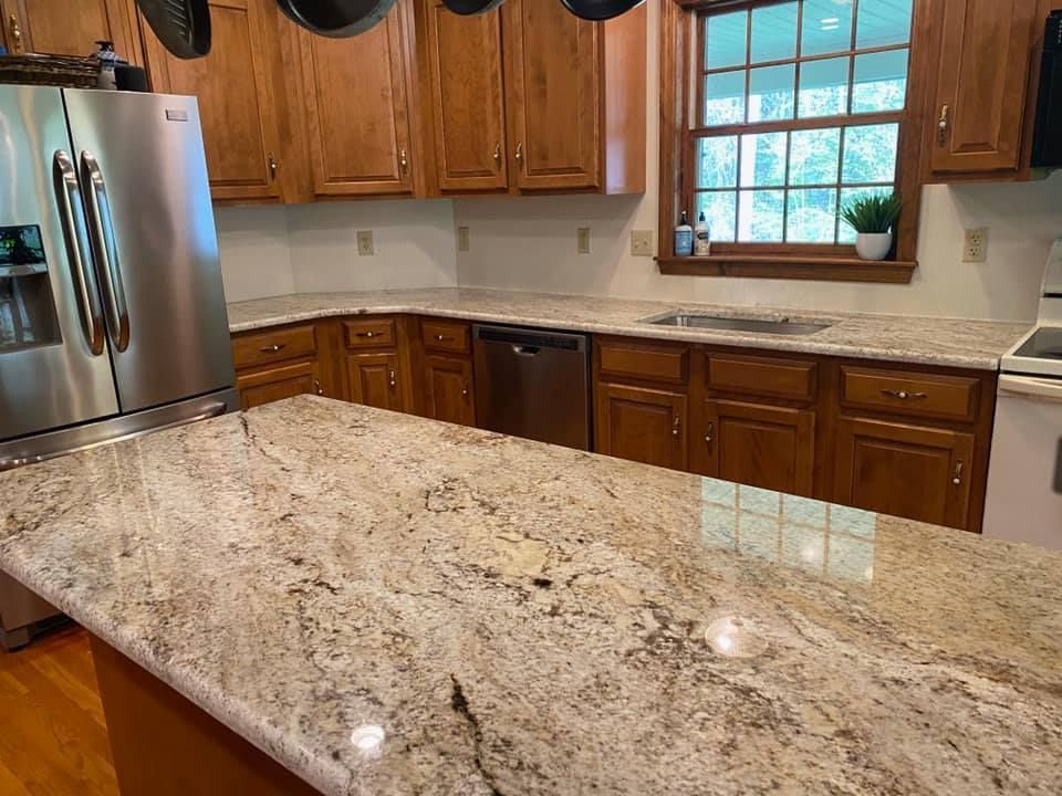 Kitchen with light-colored granite countertops, wood cabinets, stainless steel appliances, and a window overlooking greenery.