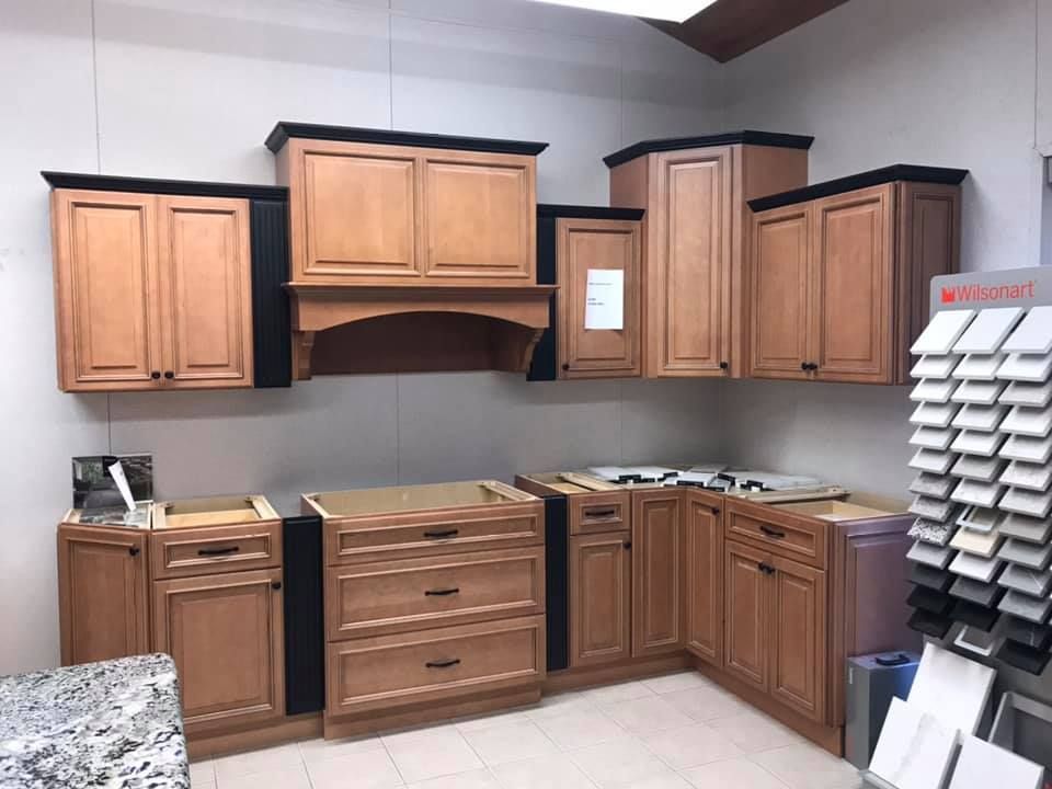 Kitchen cabinets in a showroom display, light brown with black trim, and sample materials to the right.
