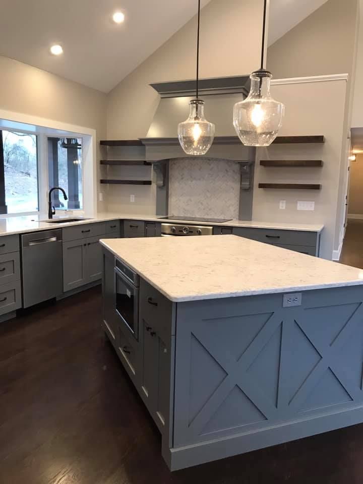 Gray kitchen with white countertops and dark wood floors. Island with an X design, open shelves, and pendant lights.