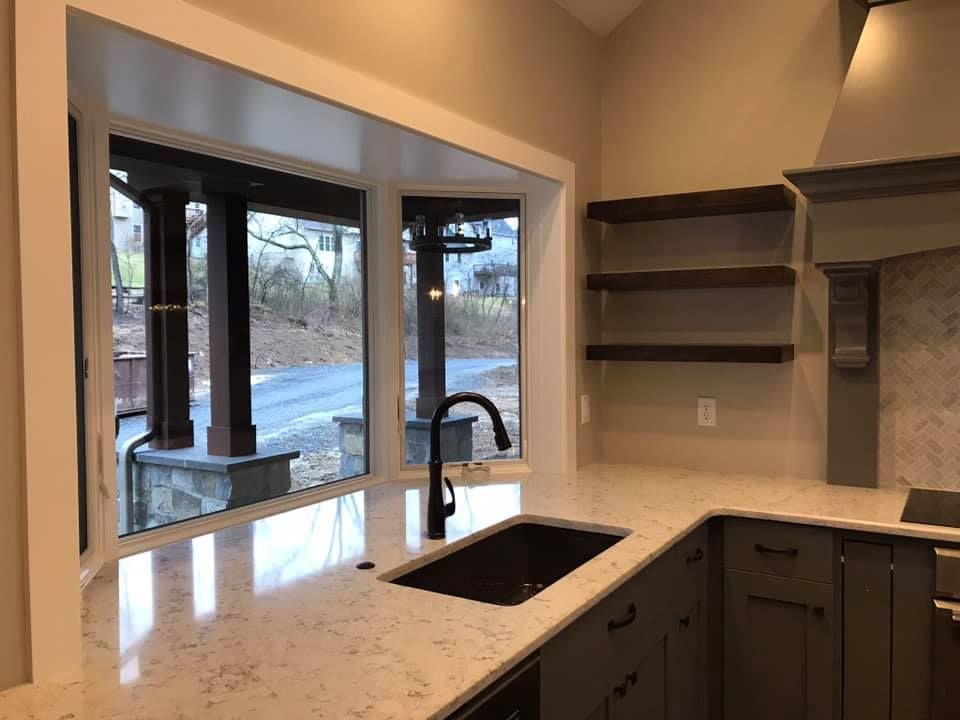 Kitchen with a bay window, countertop, sink, and floating shelves.