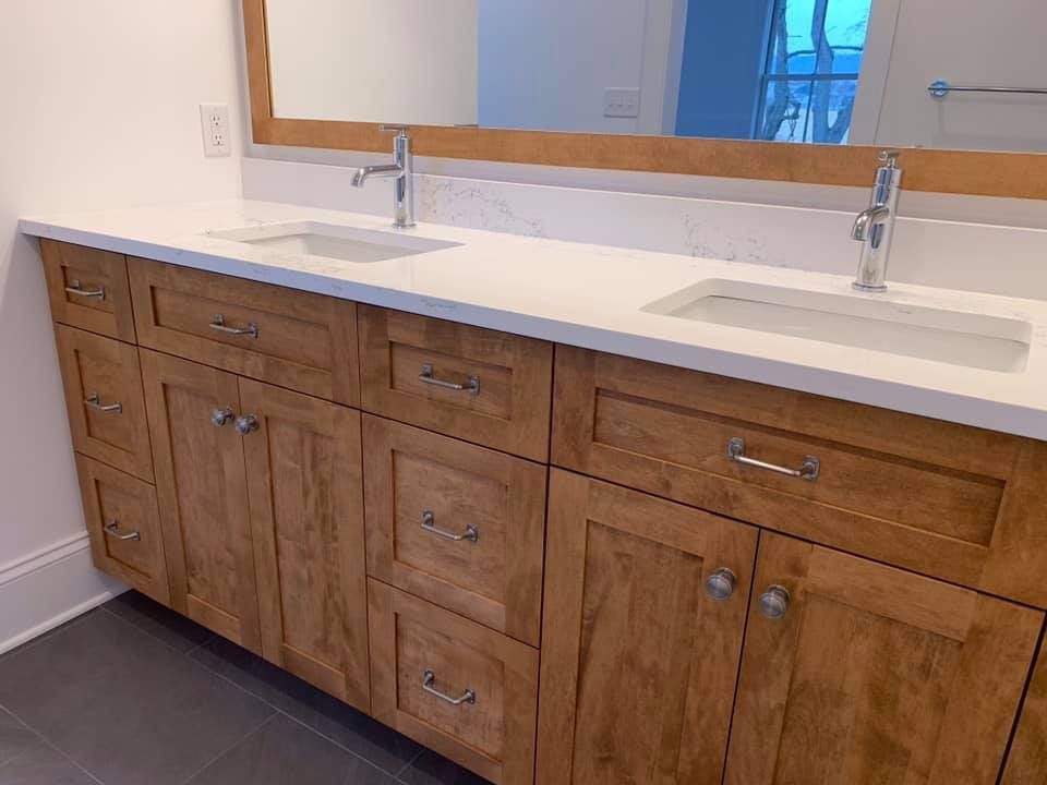 Bathroom vanity with two sinks, light wood cabinets, and a white countertop.