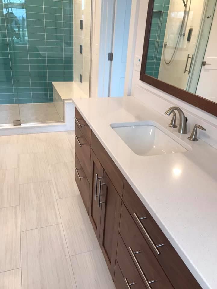 Bathroom with brown vanity, white countertop, and teal tiled shower.