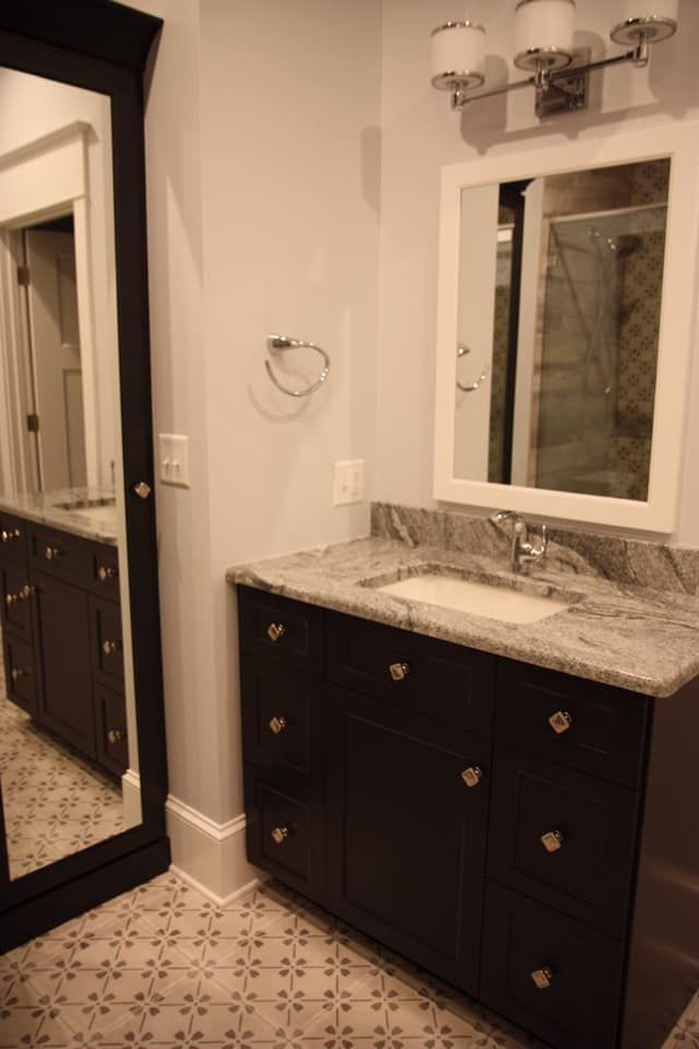Bathroom with dark brown vanity, granite countertop, large mirror, and patterned tile floor.