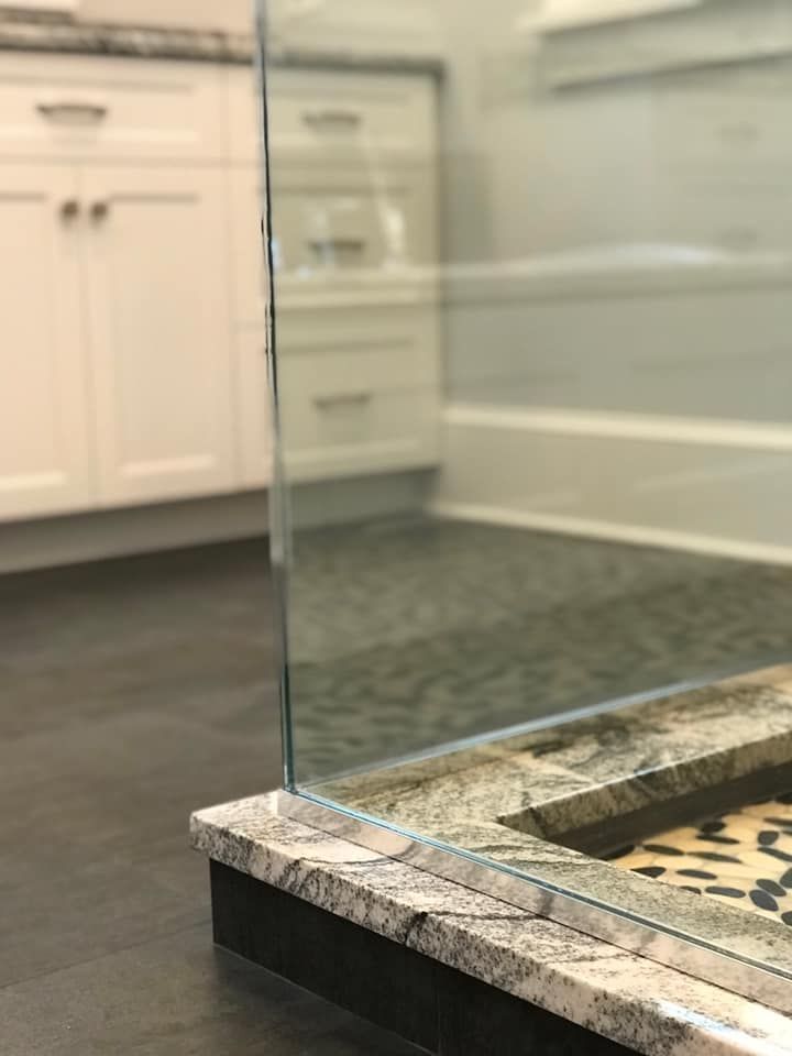 Glass shower door with granite base and dark floor. White cabinets visible in background.