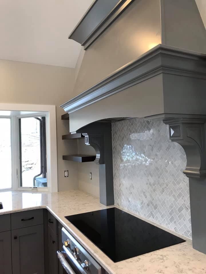 Gray kitchen range hood with tile backsplash above a black stovetop.