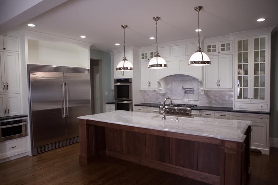 Kitchen with white cabinets, stainless steel refrigerator, island with a dark wood base, and three pendant lights.
