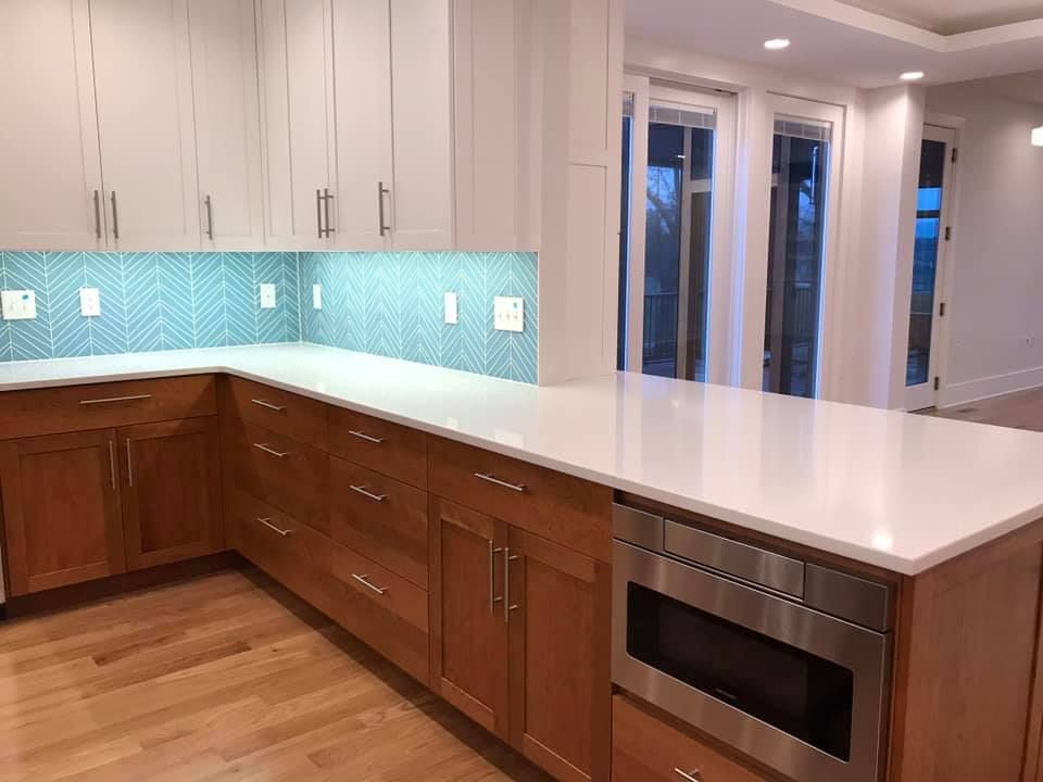 Kitchen with light wood cabinets, white countertops, and blue tile backsplash.