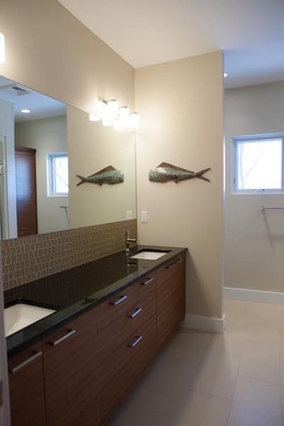Bathroom with a long wood vanity, two sinks, mirror, fish décor, and beige walls.