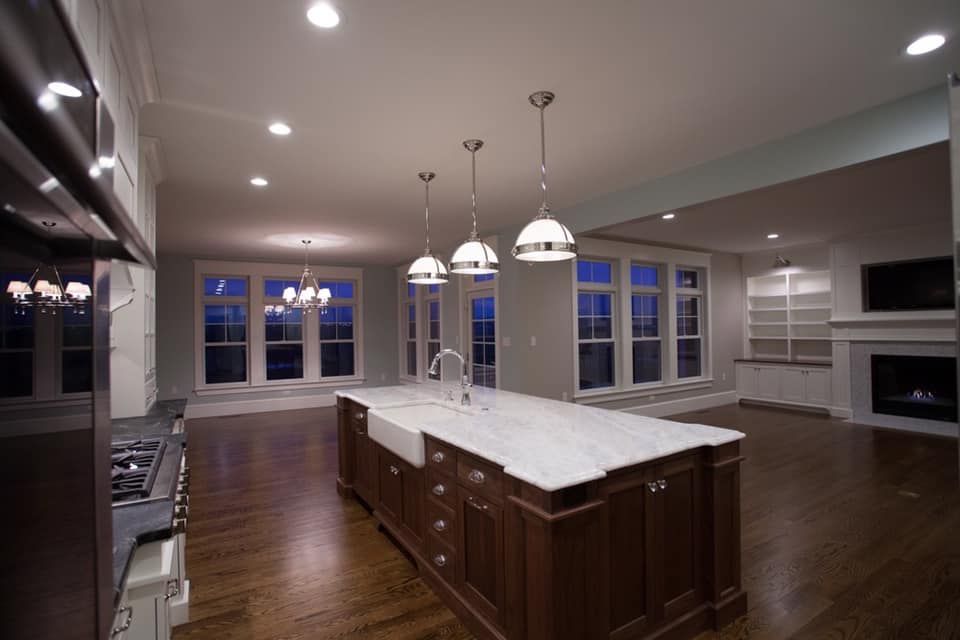 Spacious kitchen with dark wood island, white countertop, pendant lights, and large windows overlooking the outdoors.