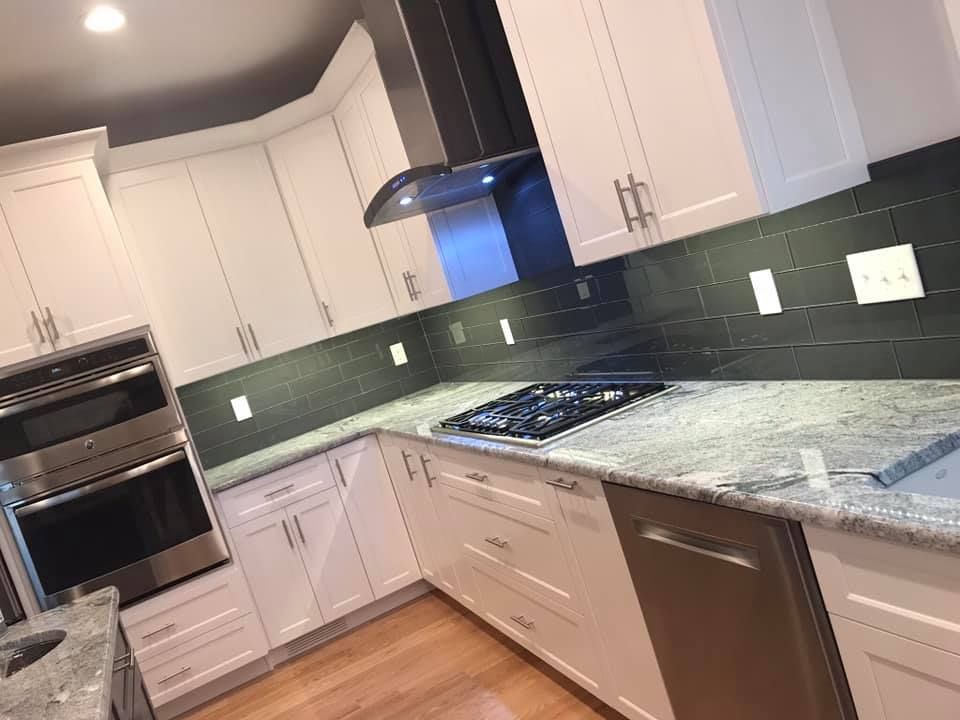 White kitchen with stainless steel appliances, dark backsplash, and granite countertops.