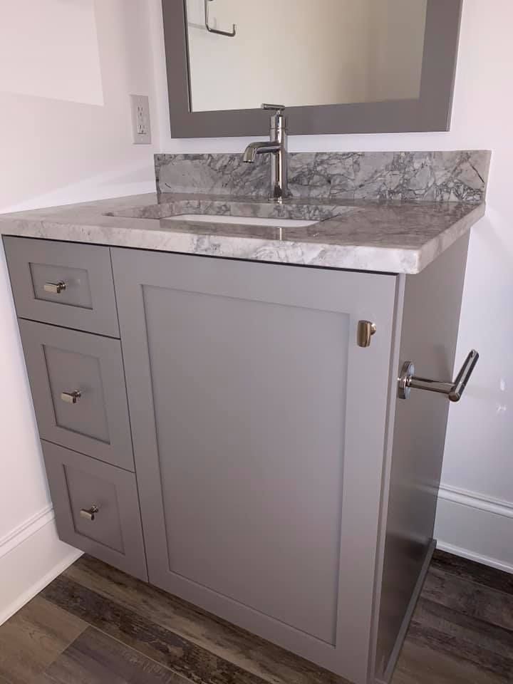 Gray bathroom vanity with granite countertop, sink, and mirror. Three drawers on the left, towel rack on the right.