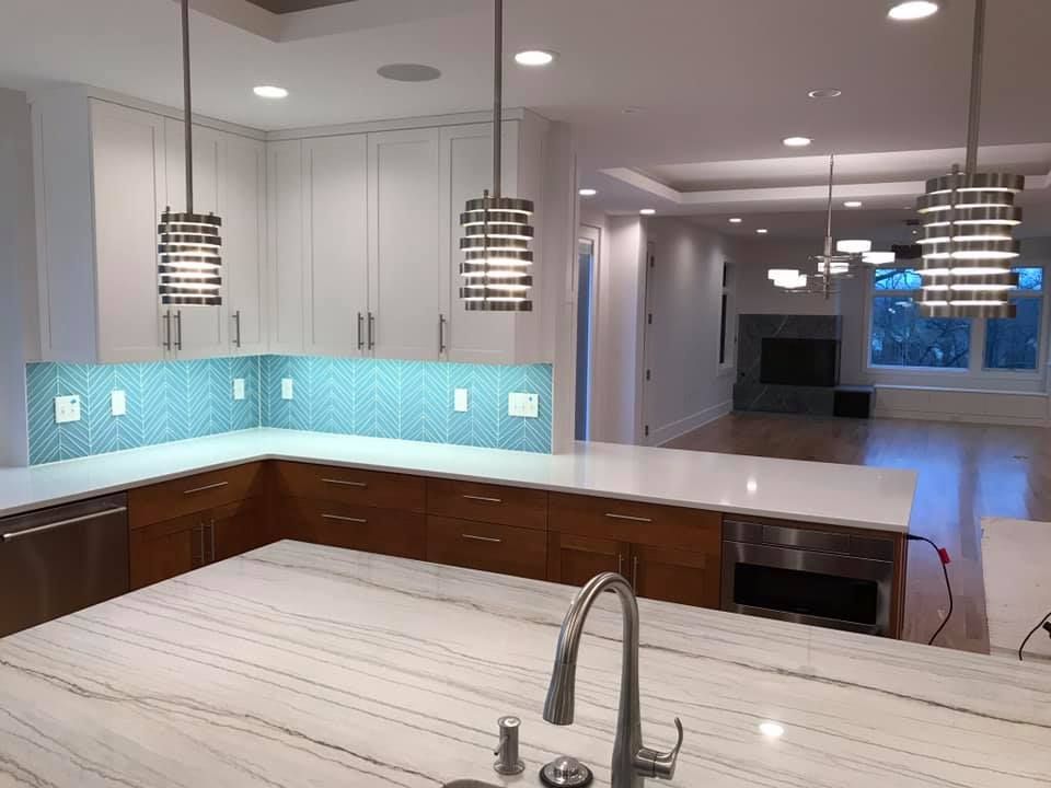 Modern kitchen with white countertops and cabinets, blue tile backsplash, and hanging lights.