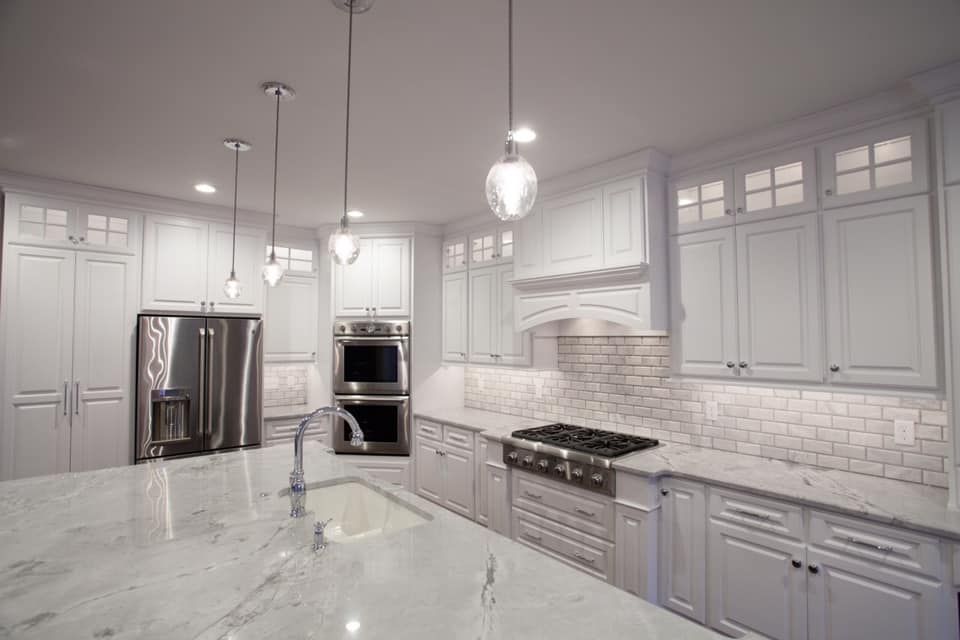 White kitchen with island, stainless steel appliances, white cabinets, and pendant lights.