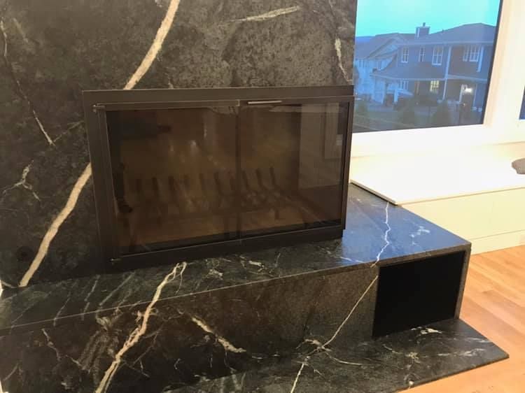 Black marble fireplace with glass doors, set against a window with a house view.