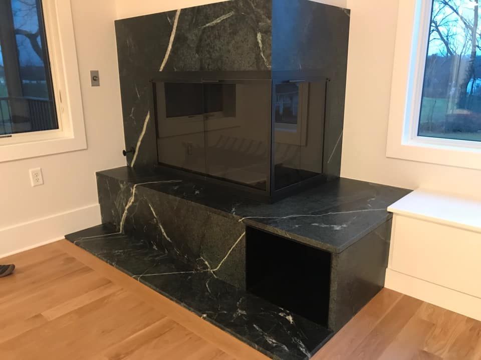 A modern fireplace constructed of black marble, with light veining. It is in a room with hardwood floors.