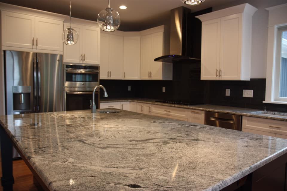 Modern kitchen with granite island, white cabinets, stainless steel appliances, and dark backsplash.