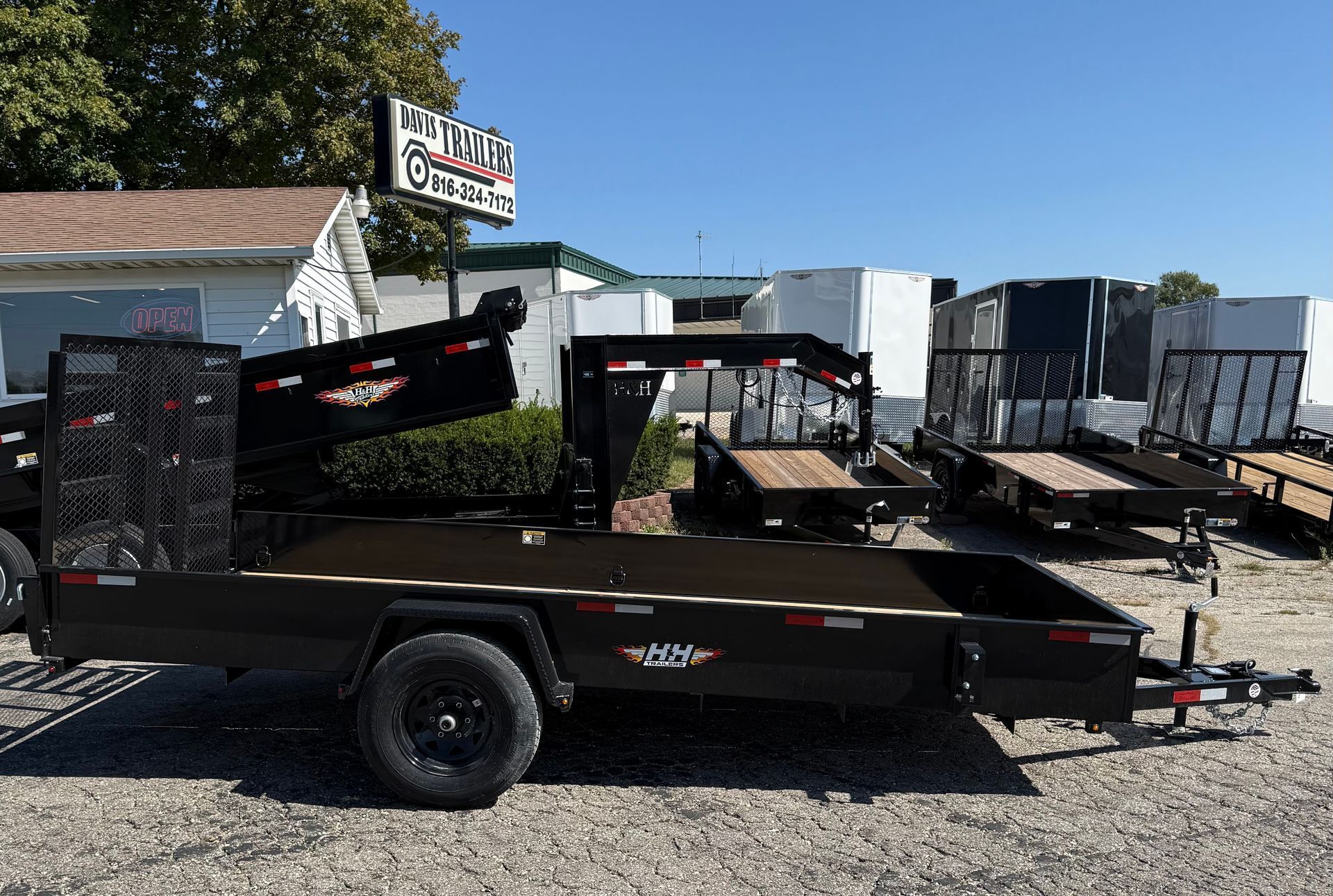 Black dump trailer parked in a lot, with other trailers and a sign for