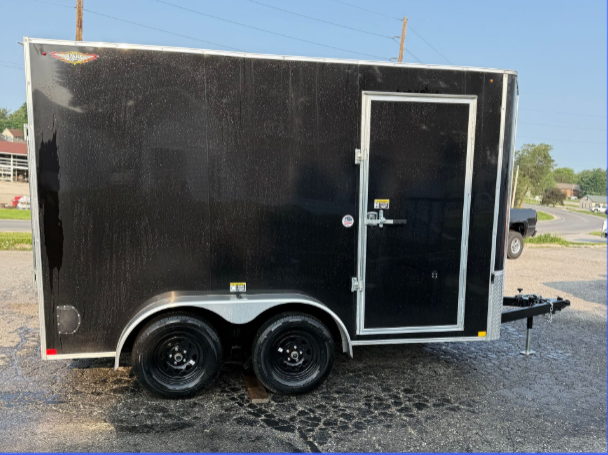 Black dump trailer on gravel in front of a building
