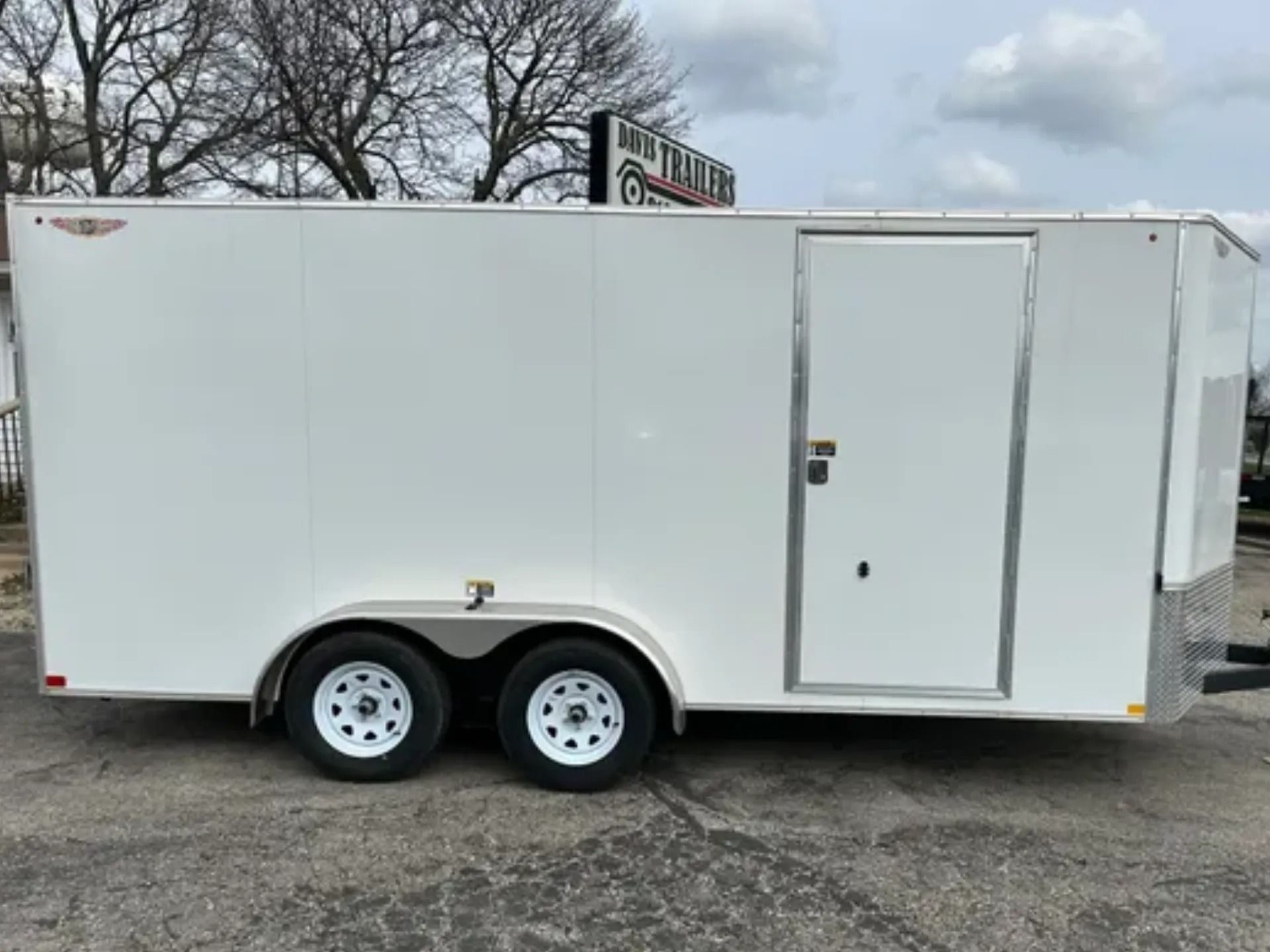 White enclosed cargo trailer with a side door, parked on pavement