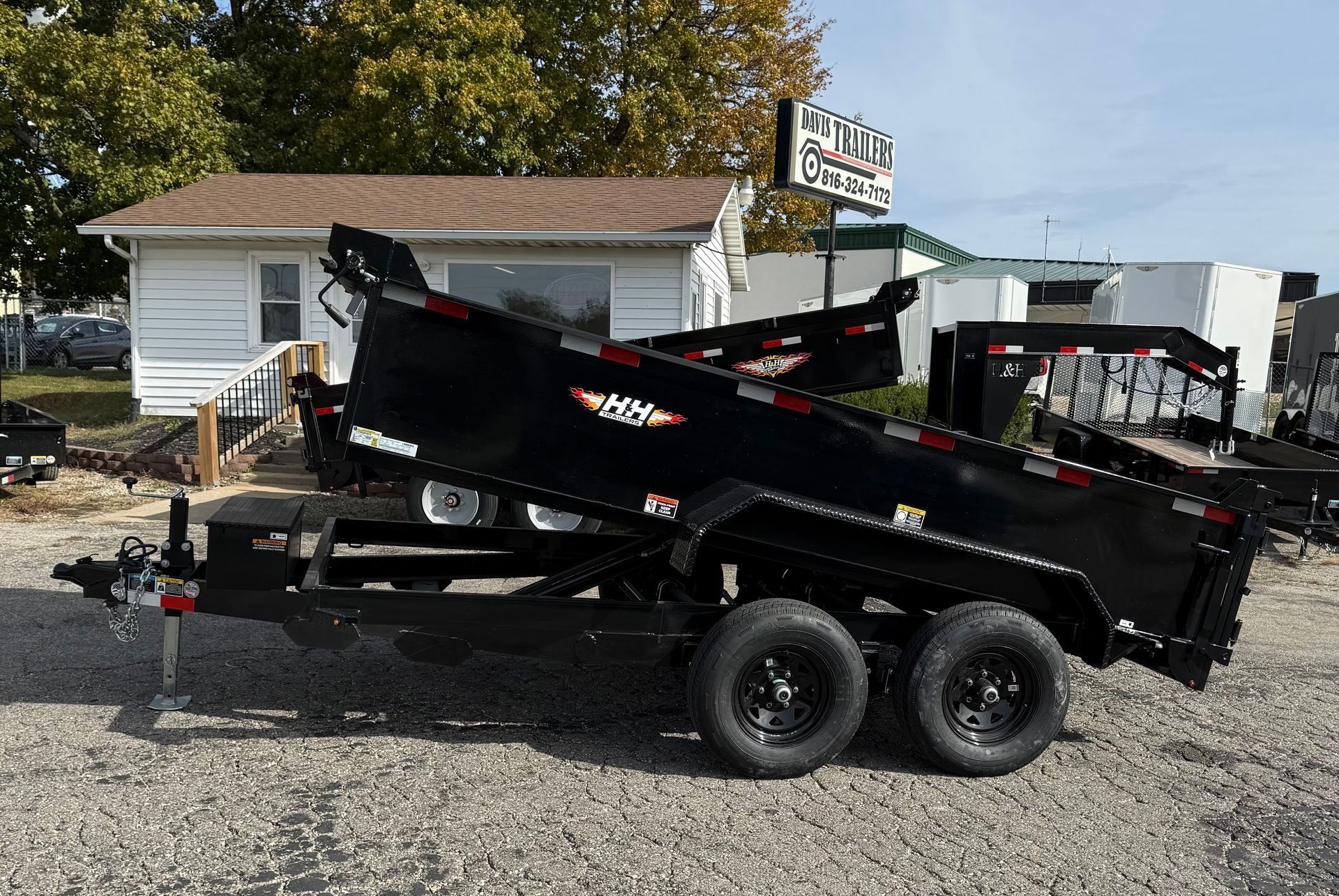 Black dump trailer tilted up, parked outside a building on a sunny day.