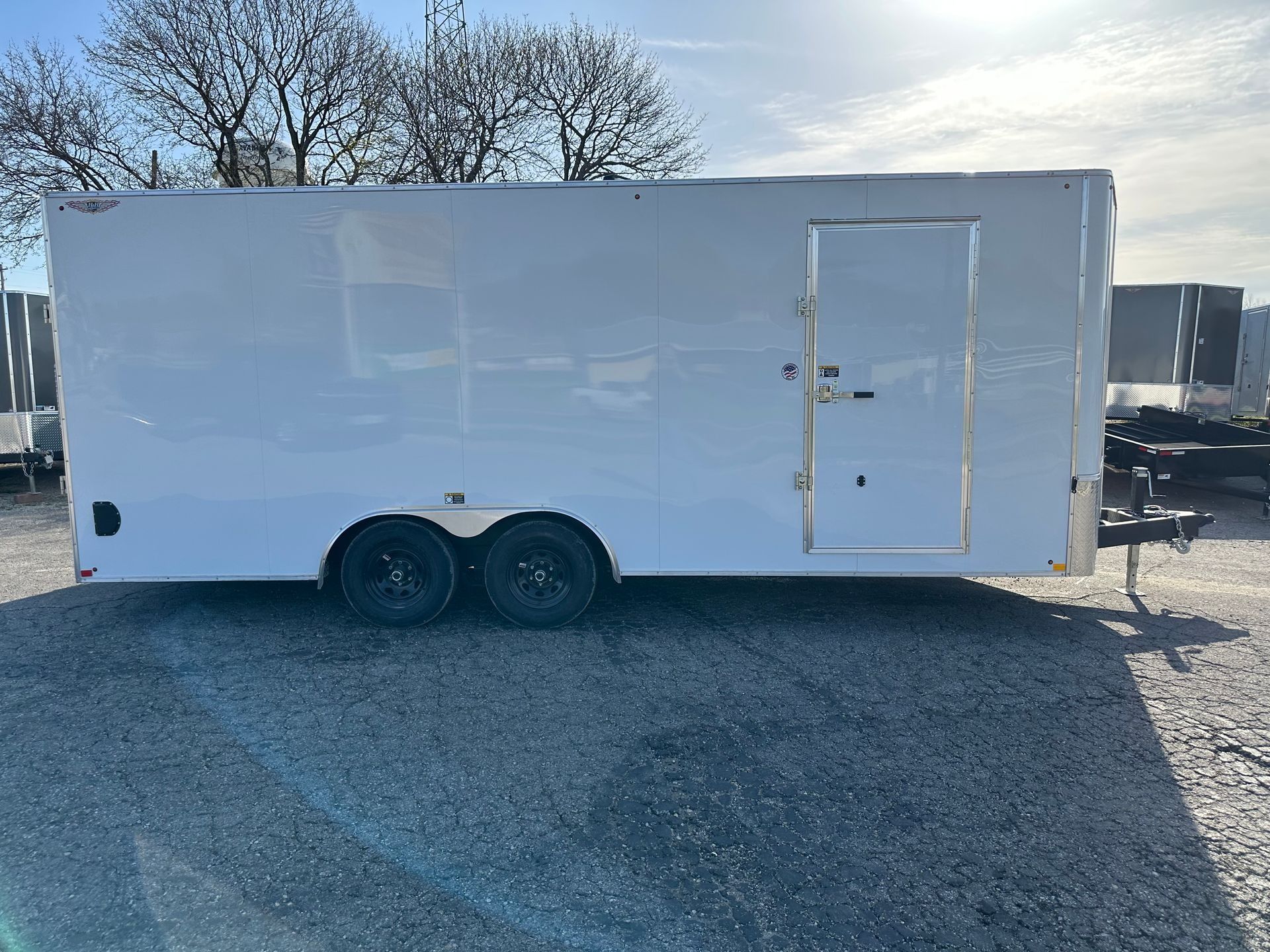 White enclosed trailer with black wheels parked on gravel.