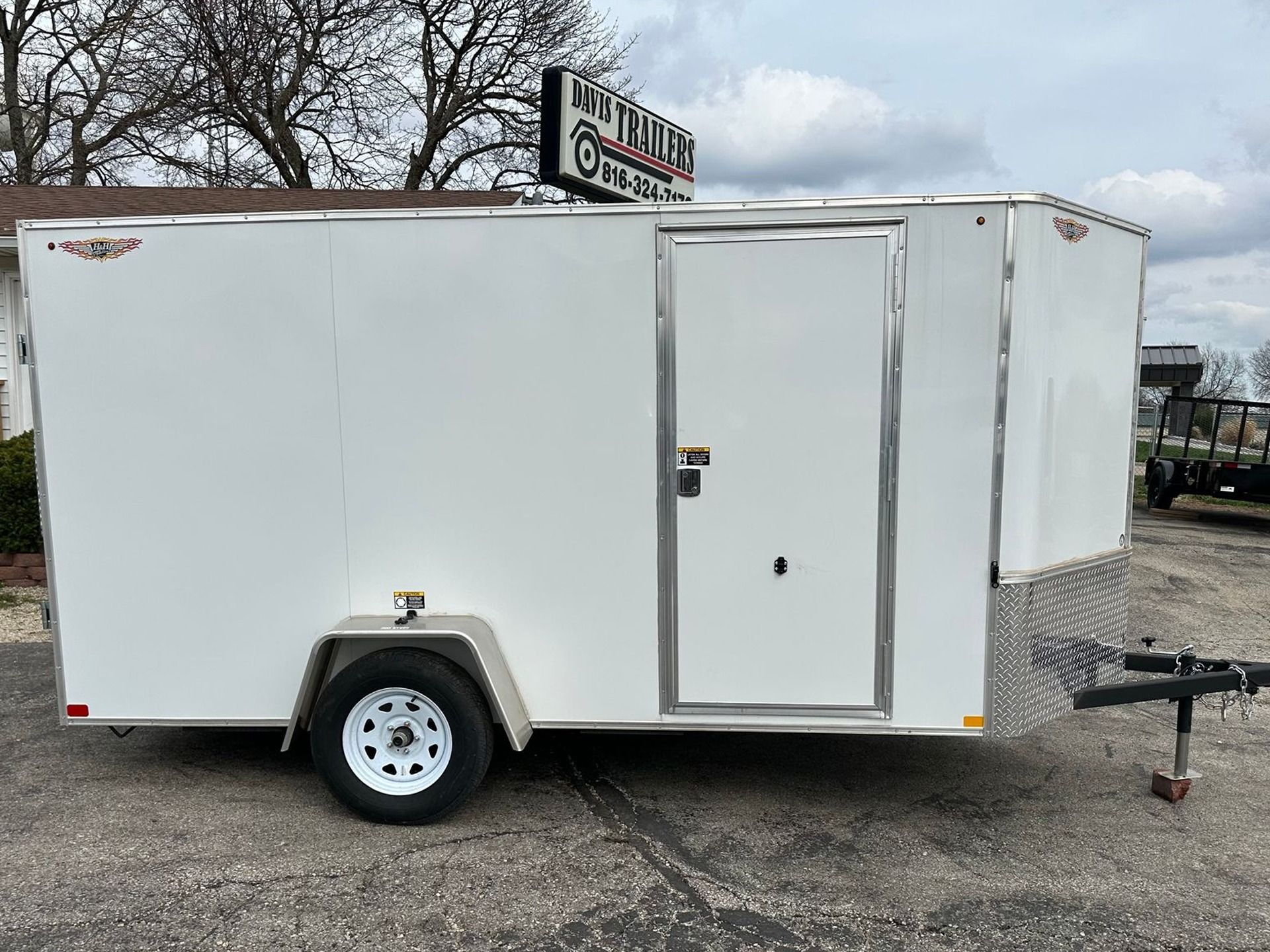 White enclosed cargo trailer on a paved lot with a dealership sign.
