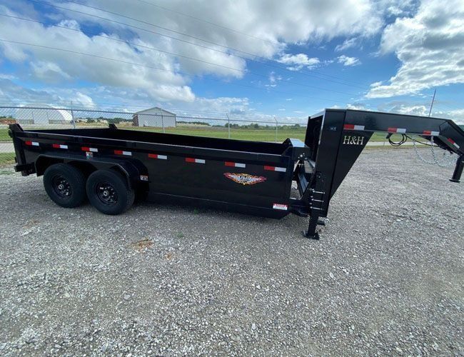 Black dump trailer on gravel under a blue sky.
