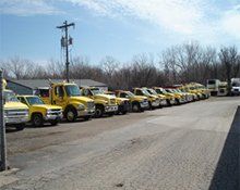 A row of yellow utility trucks parked in a gravel lot under a clear sky.