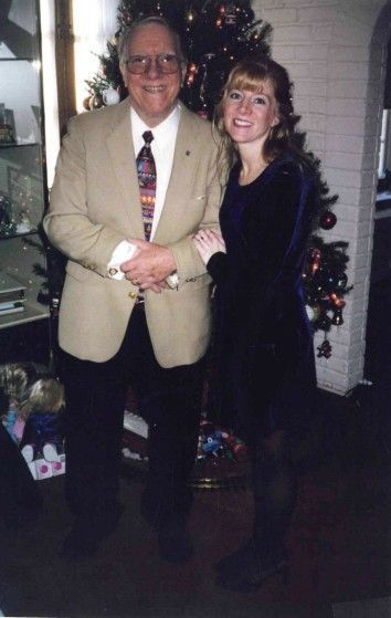 Man in blazer and woman in dress pose by Christmas tree.