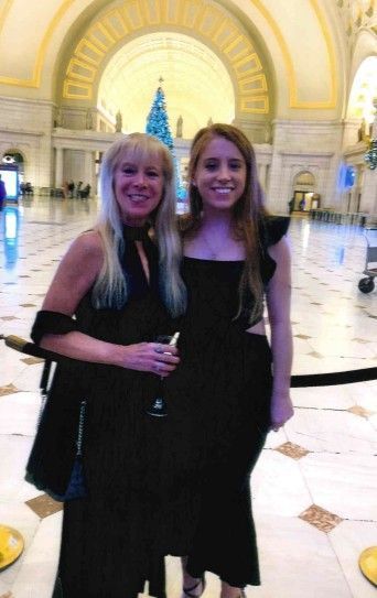 Two women smiling, posing for a photo in a grand hall with a Christmas tree.