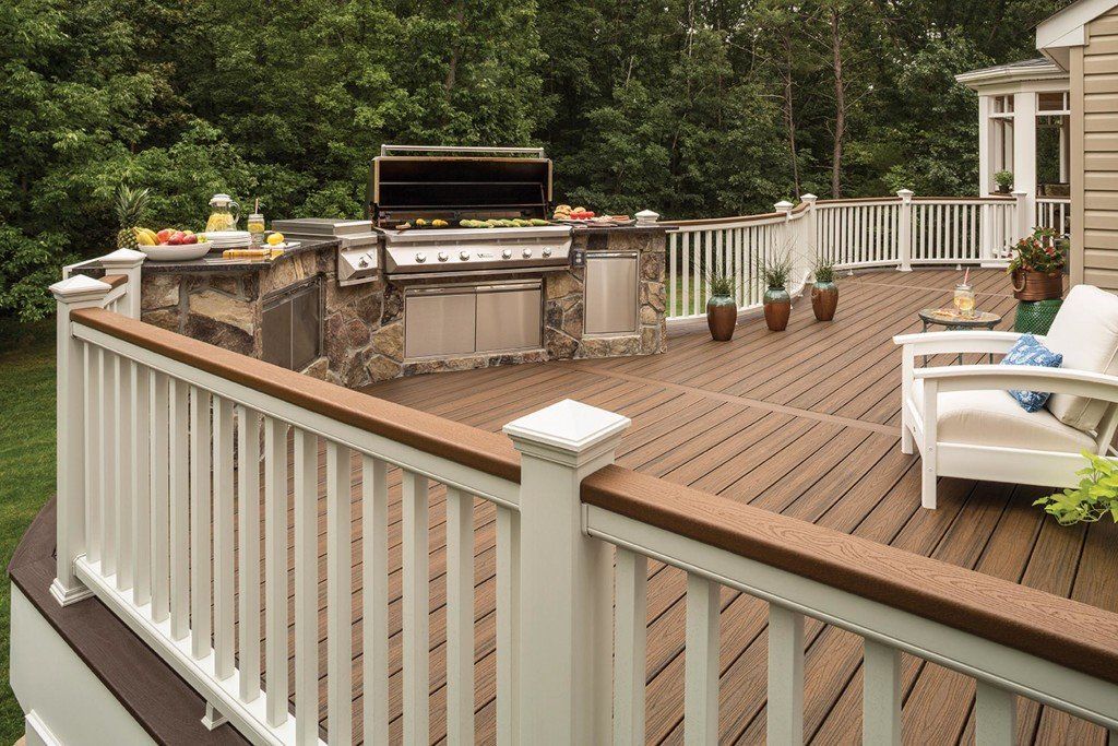 Wooden deck with white railing, built-in grill and benches, and a white lounge chair in a backyard.