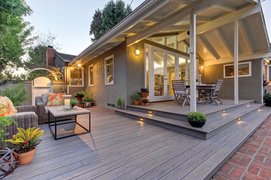 Modern backyard patio with gray deck, outdoor seating, potted plants, and warm porch lights