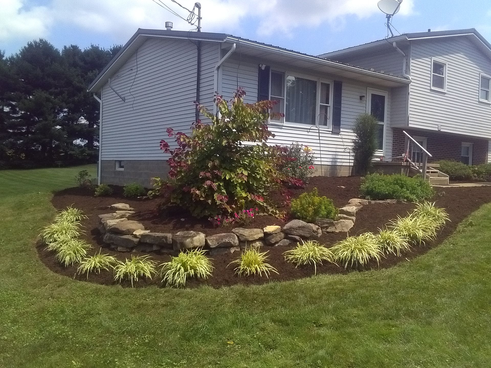White house with a landscaped flower bed and green lawn in the front yard