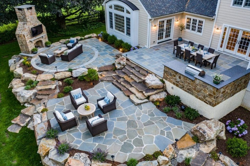 Outdoor patio with stone seating, steps, and a built-in fireplace beside a house