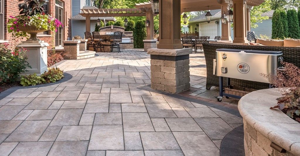 Stone patio walkway with pergola, potted flowers, and built-in benches in a landscaped courtyard
