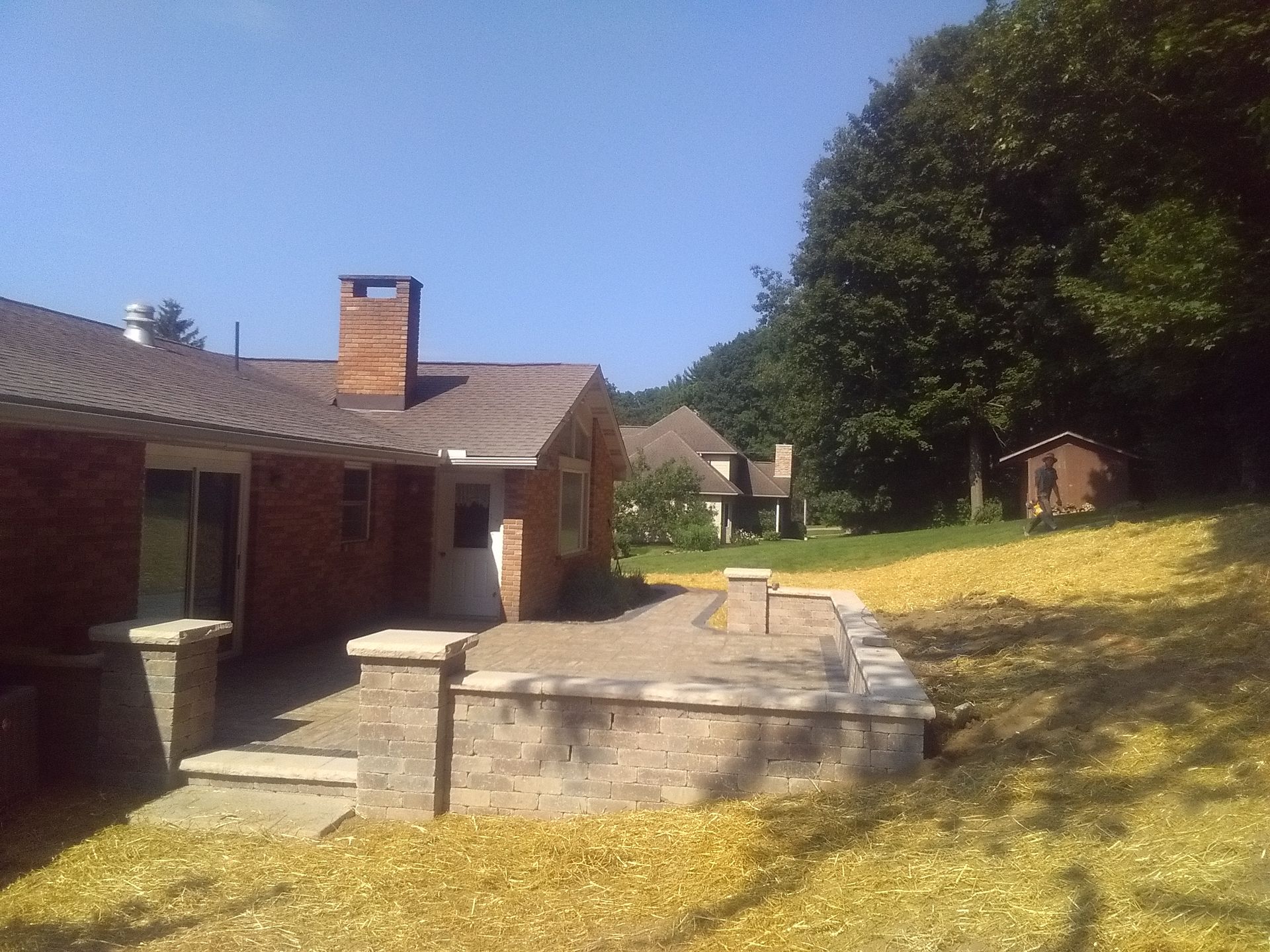 Backyard patio with brick house, stone steps, and a large tree on a sunny day