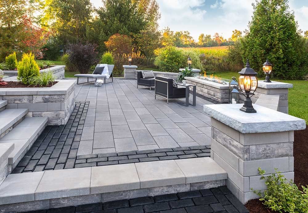 Stone patio with built-in seating and lanterns in a landscaped garden at dusk