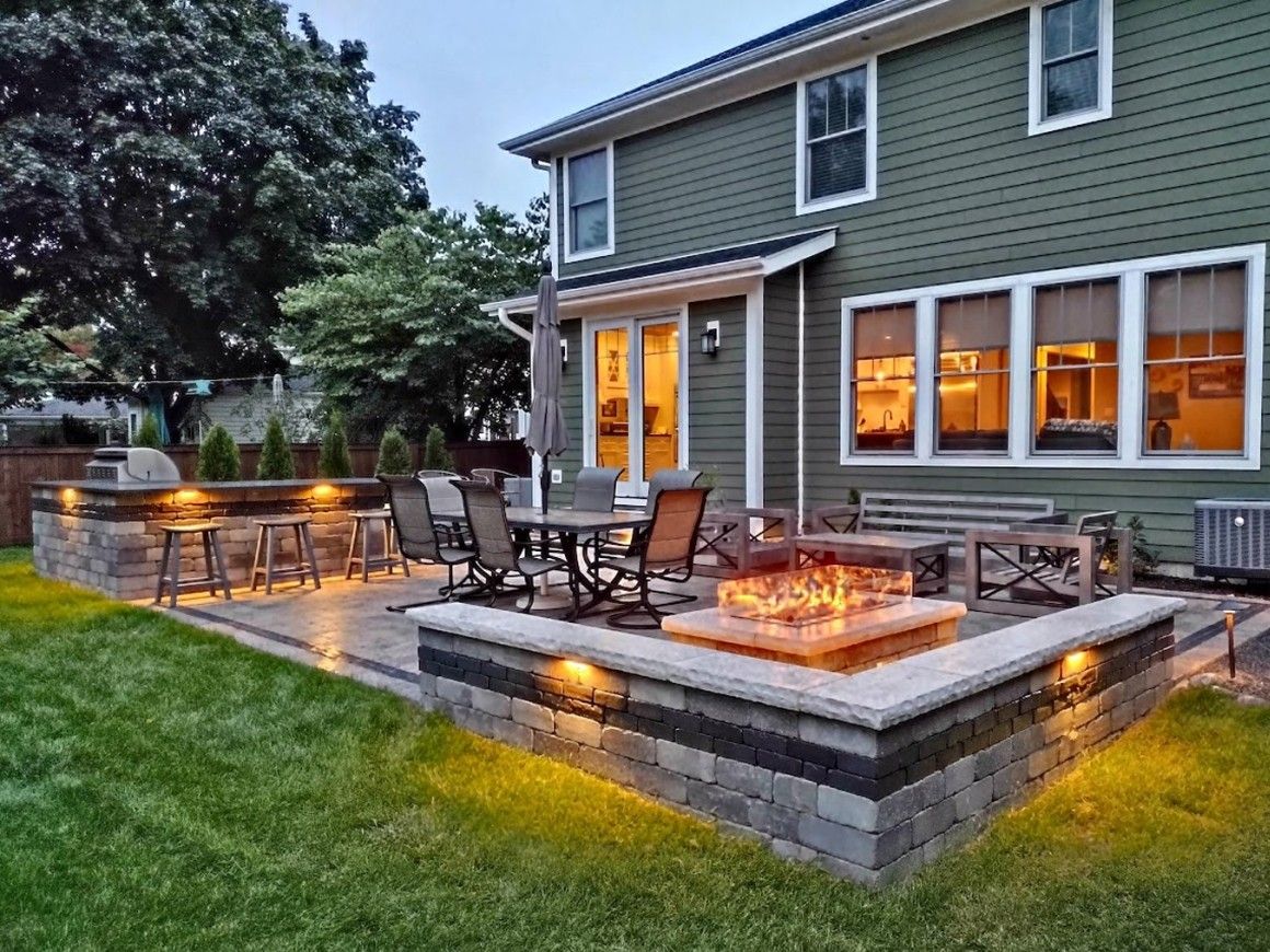 Modern house with a lit patio, outdoor dining set, and fire pit at dusk